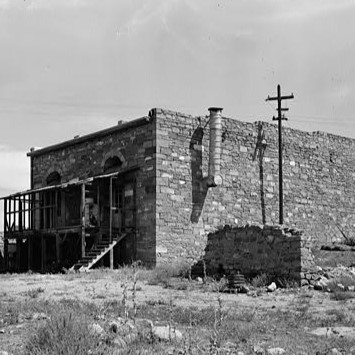 Stone building with external staircase and utility pole in a barren, grassy landscape.