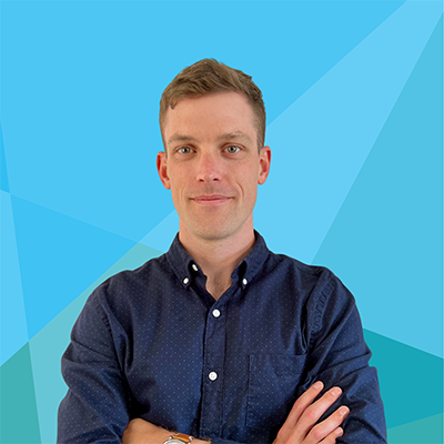 Man with short brown hair in a blue shirt standing with arms crossed against a blue geometric background.